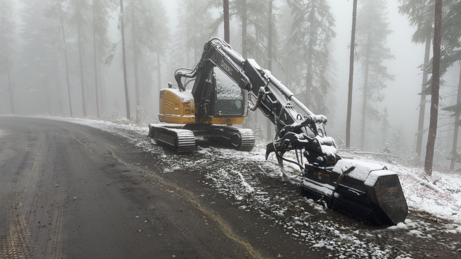 Snow-covered John Deere harvester with a processing head working a winter timber unit